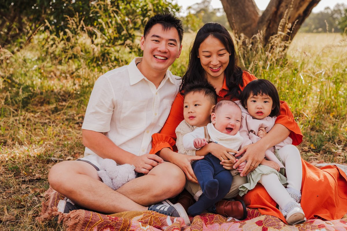 Andrea Goh with her husband and three young children, sitting together on a picnic blanket